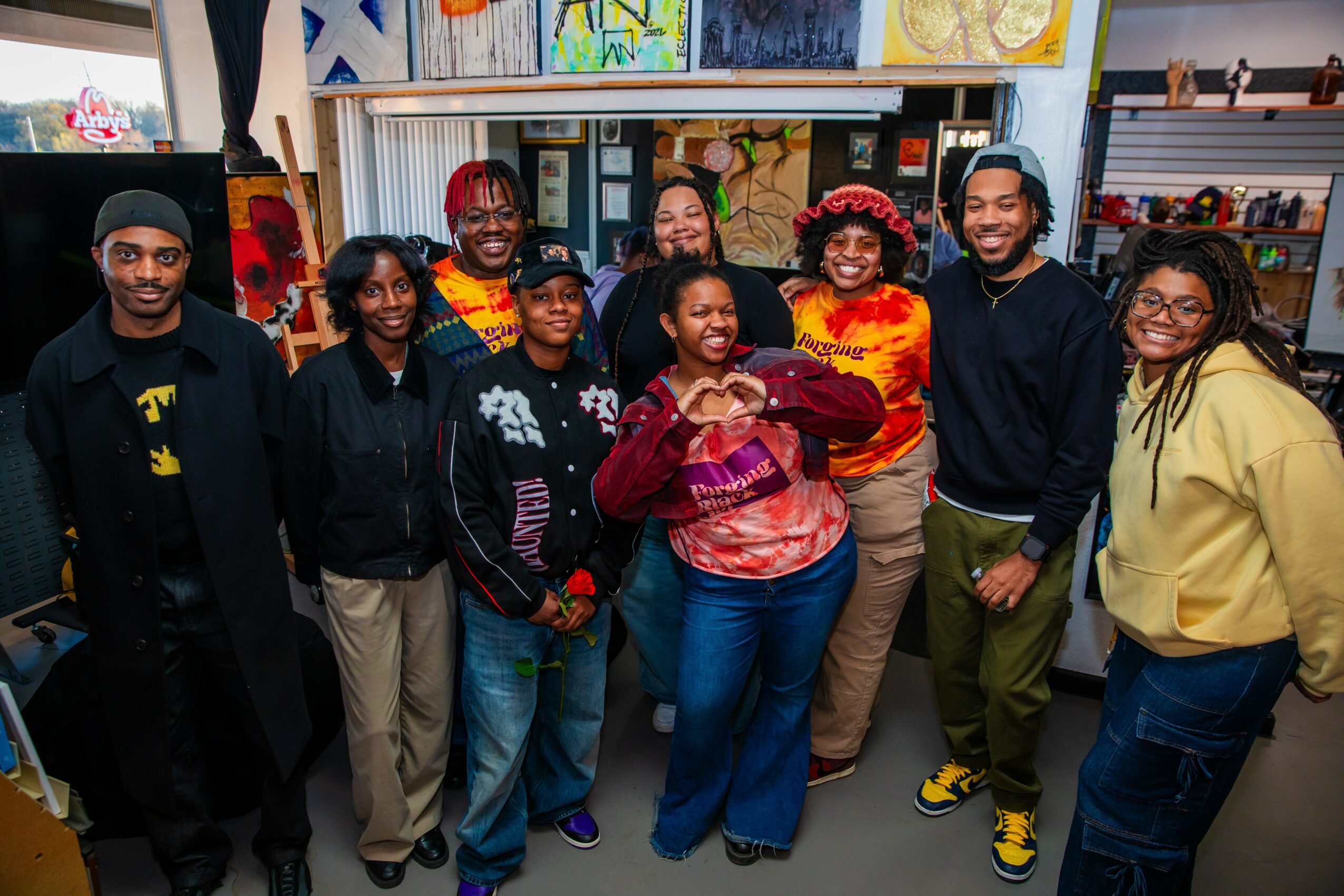 Group of nine diverse people standing inside an art store, smiling and posing for the photo.