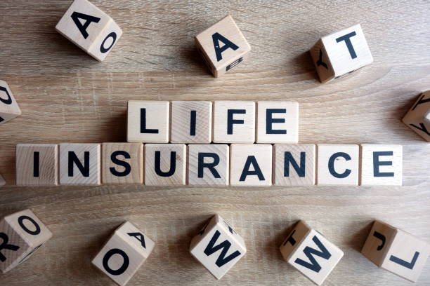 Wooden blocks spell out 'LIFE INSURANCE' on a wooden surface with some blocks scattered around.