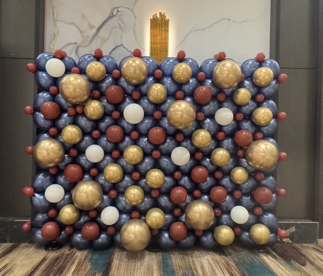 Decorative display with gold, white, red, and blue spherical ornaments arranged on a wall, with a gold candle at the top center.