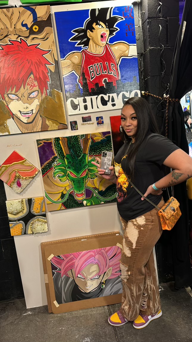 Woman standing in front of colorful artwork, holding a drink, with paintings of anime characters on the wall behind her.