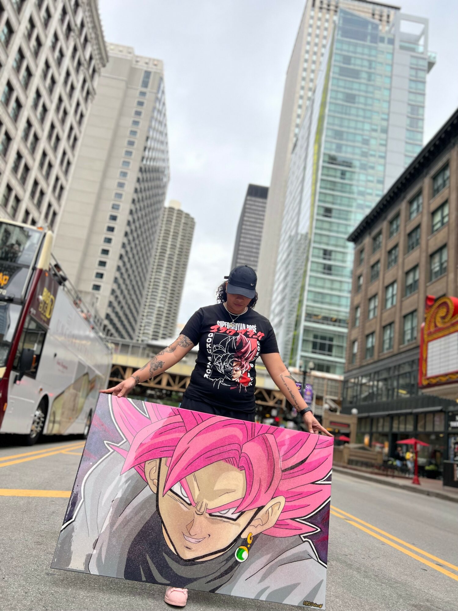 Person holding a large anime-style illustration of a character with pink hair and a serious expression, city street background.