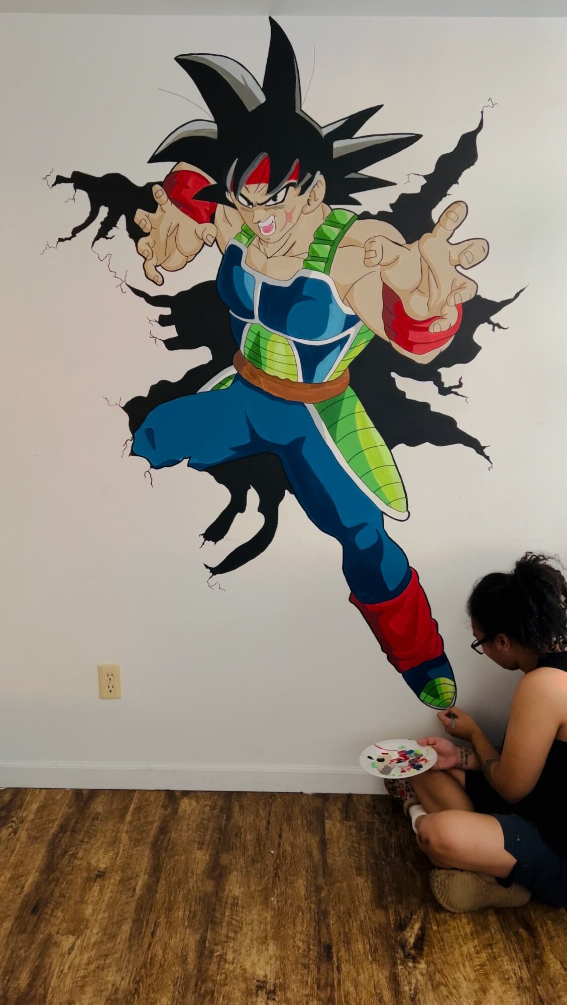 Child painting a large Dragon Ball character on the wall, with a paint palette in hand.