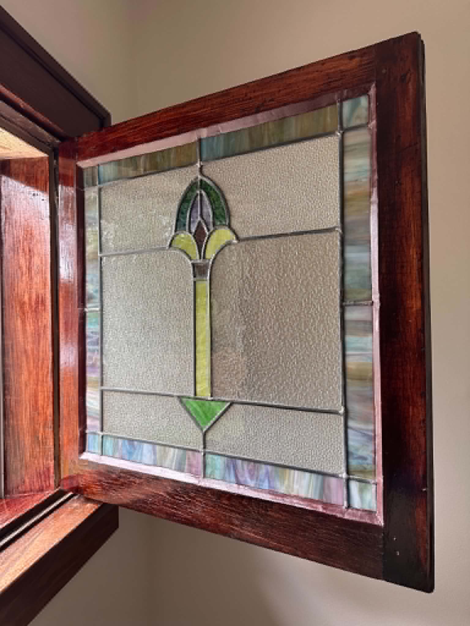 Stained glass window with geometric design and a wooden frame, viewed at an angle.