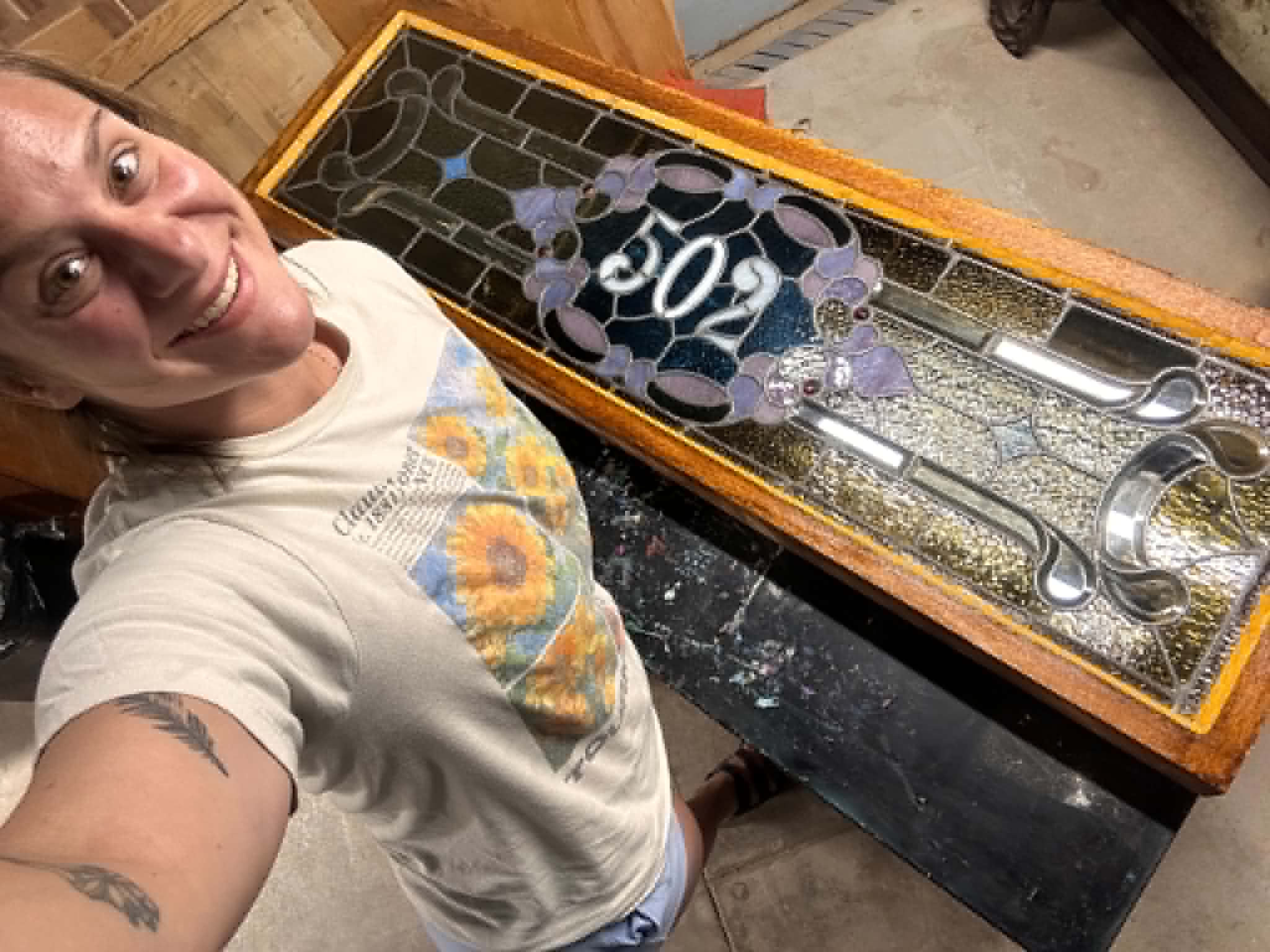 Person smiling taking a selfie next to a glass display case with tools and circular objects inside.