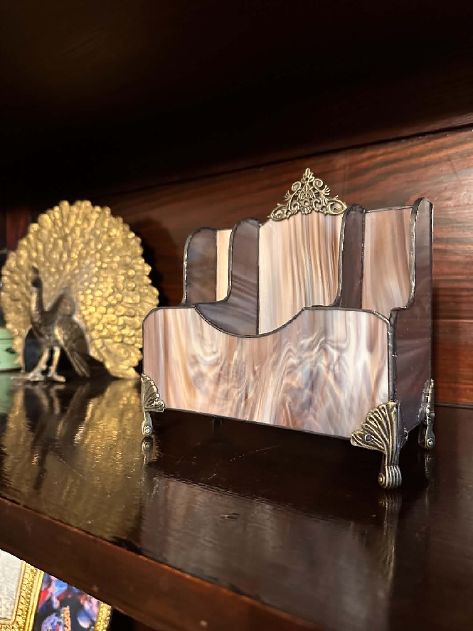 Decorative wooden and metal bookend with ornate design, placed on a dark wooden surface, with a gold-colored decorative object nearby.