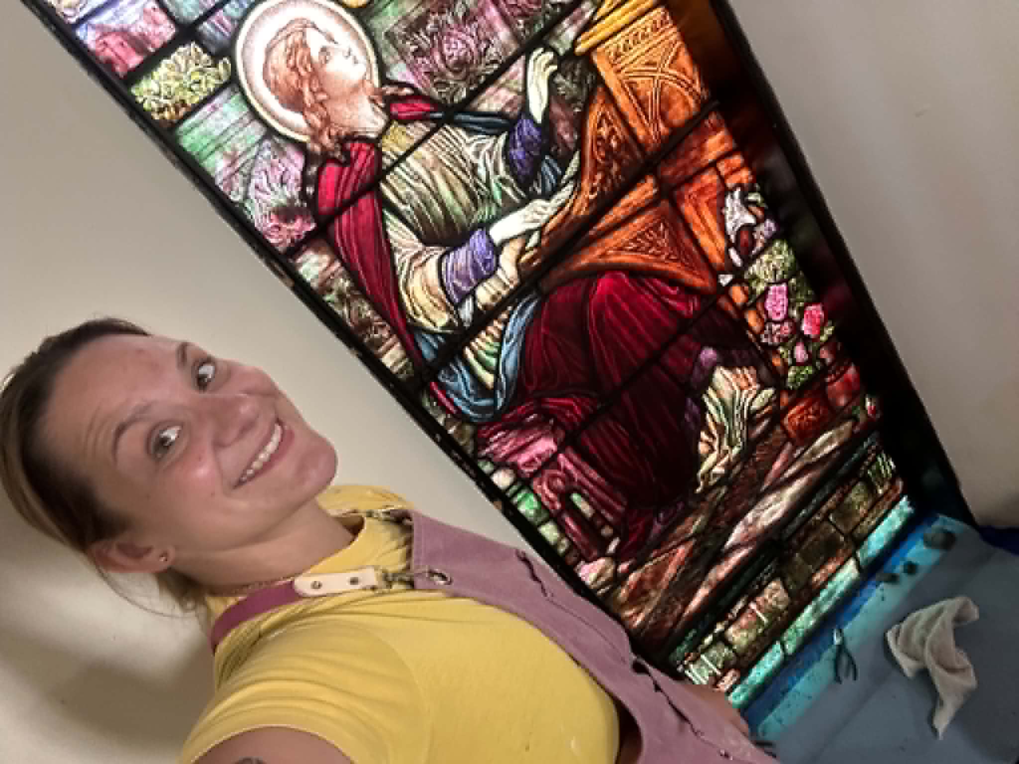 Woman smiling in front of a stained glass window depicting a religious figure playing a musical instrument.