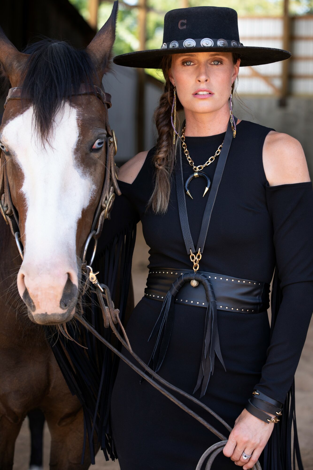 Woman with braided hair wearing a wide-brimmed hat and black outfit standing next to a horse.