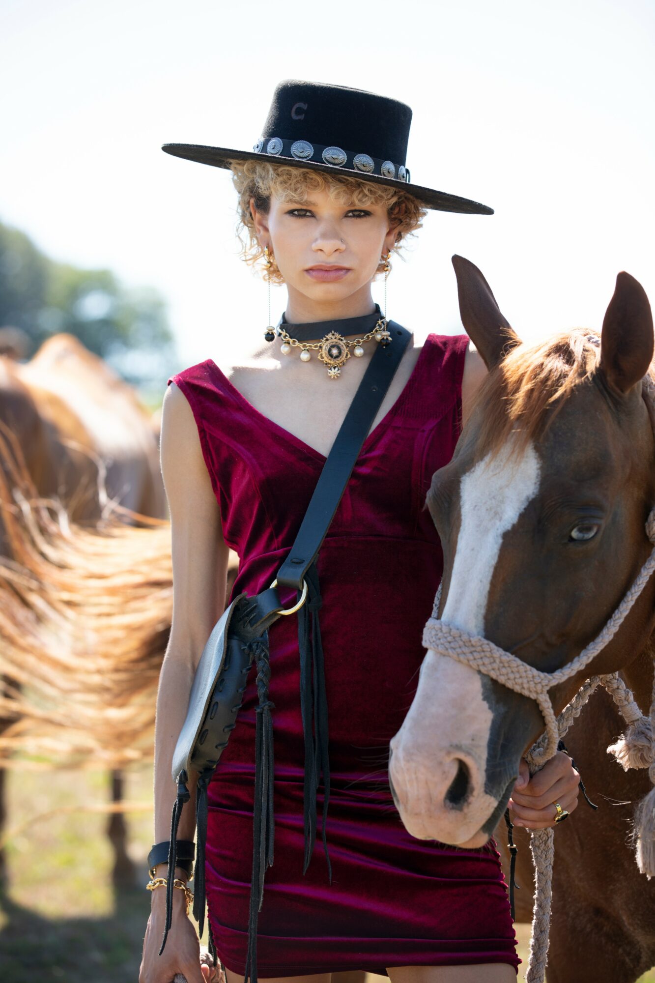 Young woman in a burgundy dress and wide-brimmed hat standing next to a horse outdoors.