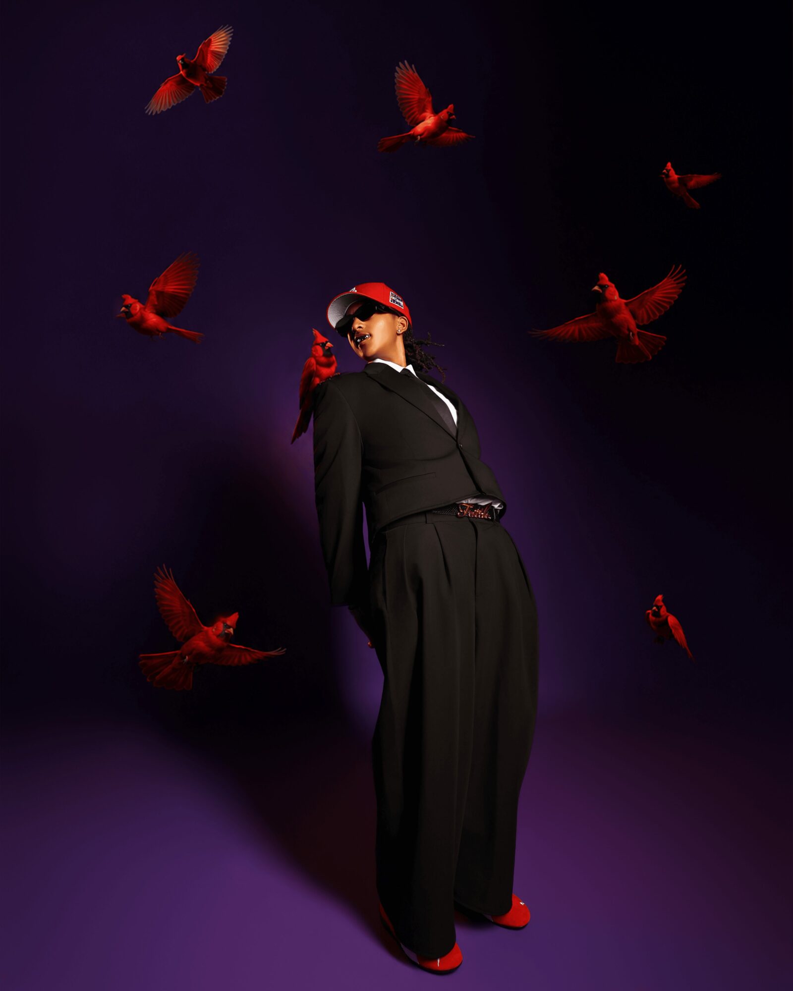 Person in black outfit with red shoes and cap, surrounded by red birds flying against a dark background.
