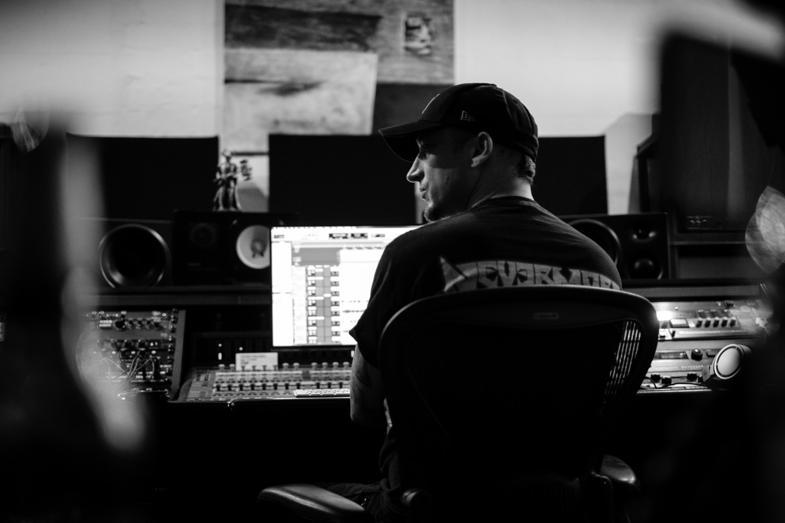 Person working at a music studio with computer screens and audio equipment, facing away from the camera, in black and white.