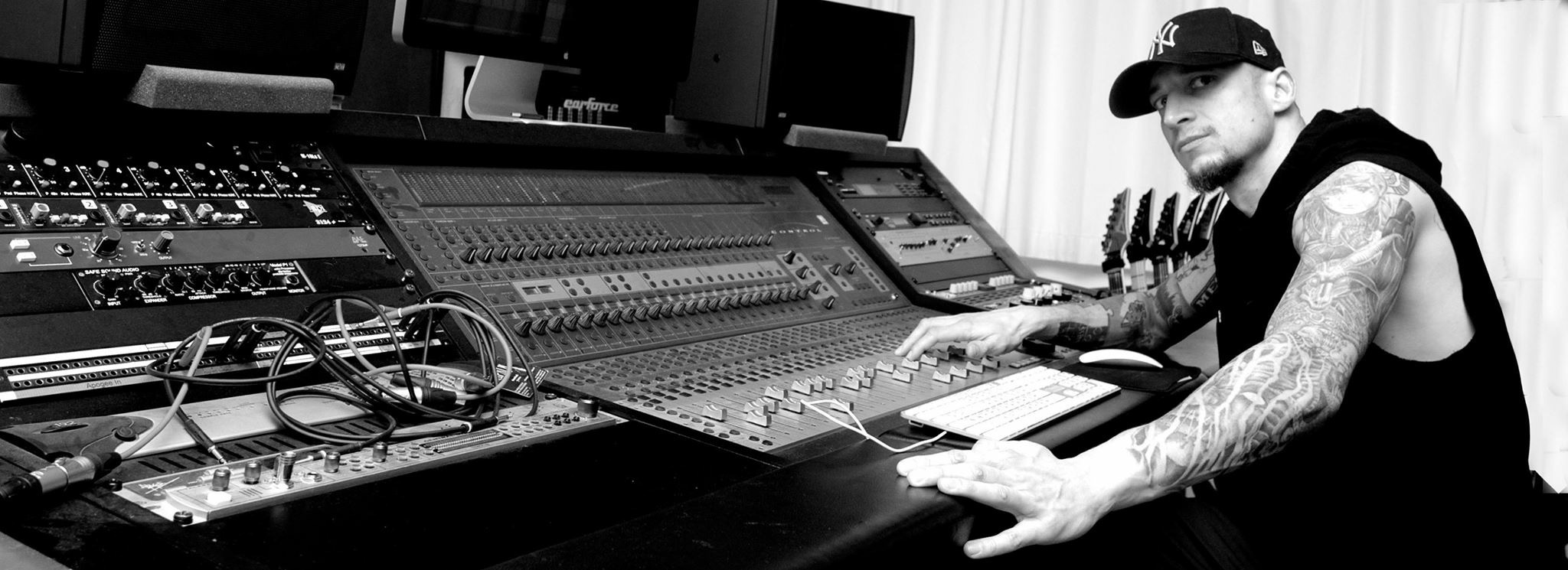 Person with tattoos wearing a cap working with audio equipment in a studio.
