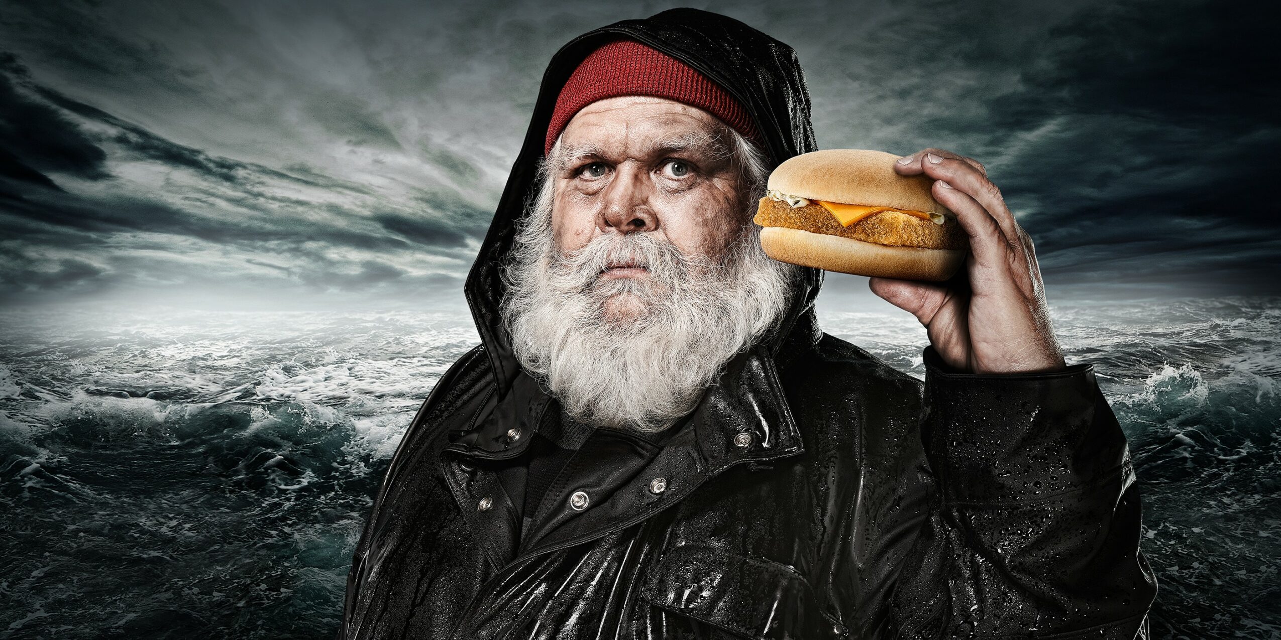 Old man with a beard holding a hot dog against a stormy sky background.