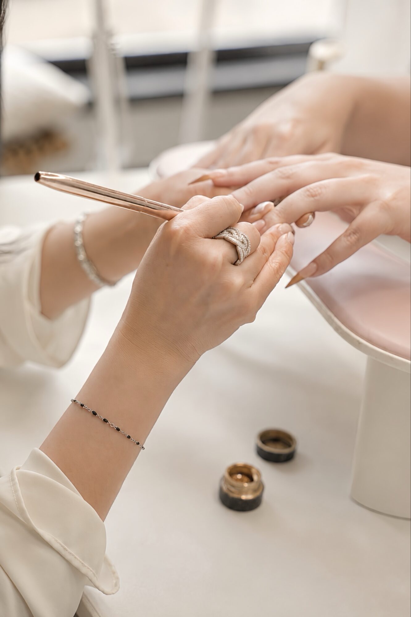 Person receiving a manicure, with hands resting on a pink cushion, and nail polish bottles nearby.