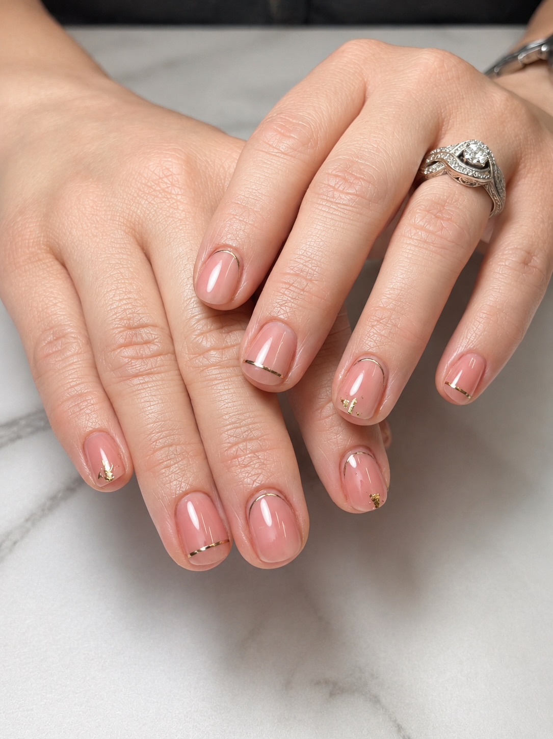 Close-up of hands with rings, resting on a marble surface, showing well-manicured nails and jewelry.