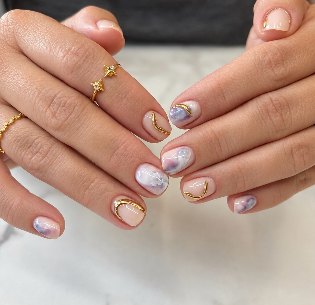 Hands with decorated nails and gold rings, featuring marble and gold accents, against a neutral background.