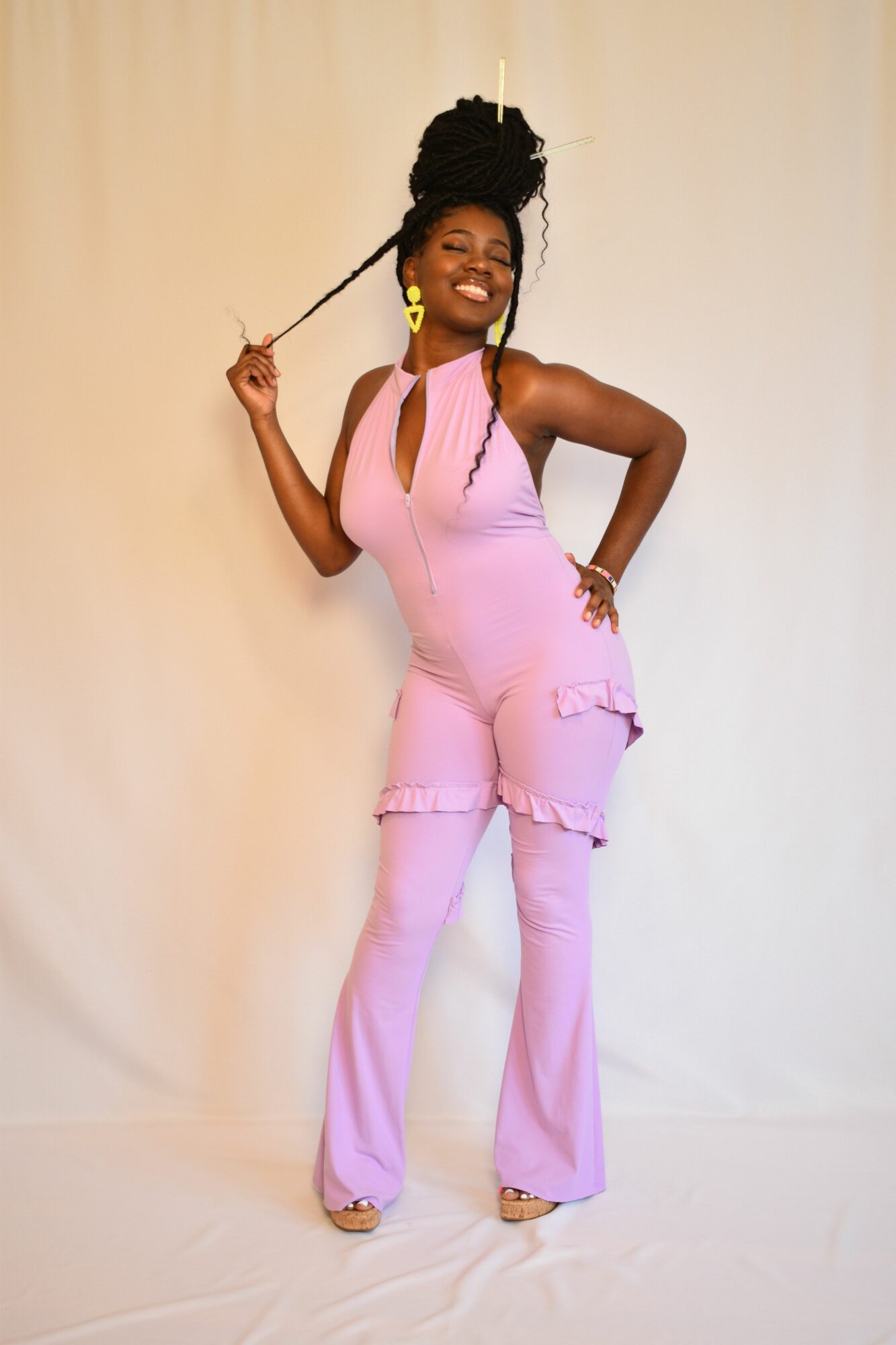 Woman in pink pants and top, smiling, holding a braid, standing against a plain background.
