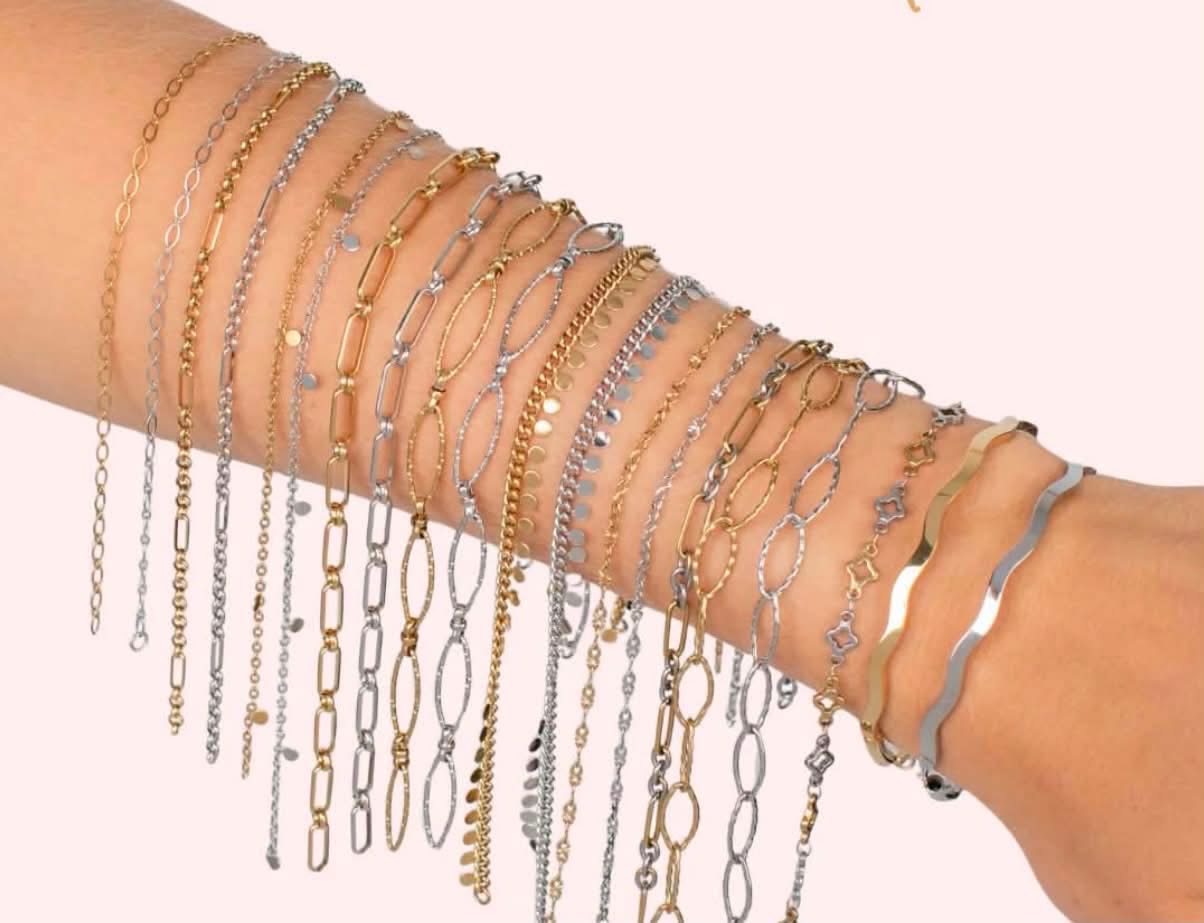 Multiple gold and silver bracelets and chains on a person's arm, with a pink background.