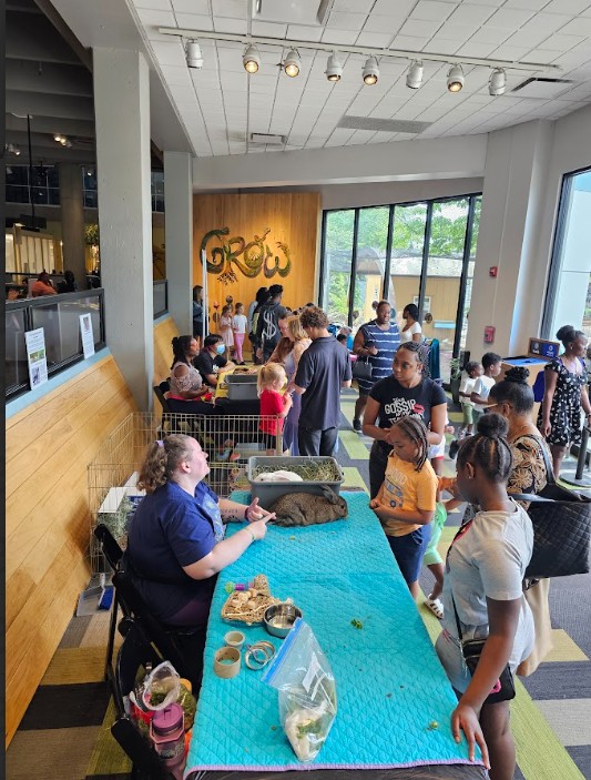 People gather around a table inside a cafe, with large windows and a wooden wall with graffiti art in the background.