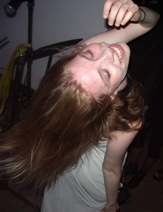 Person with long hair smiling, head tilted back, eyes closed, in a relaxed pose.