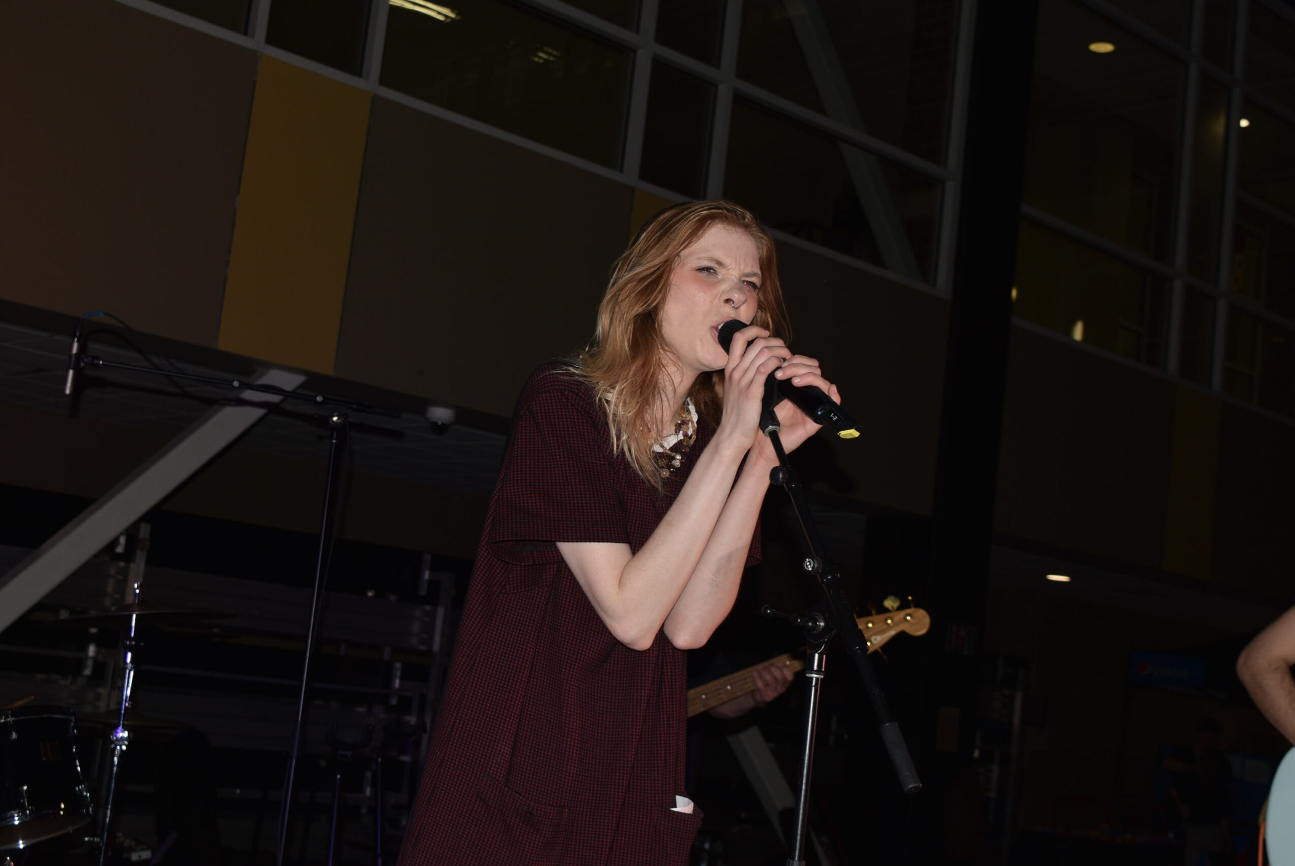 Woman singing into a microphone on stage with musical instruments in background.