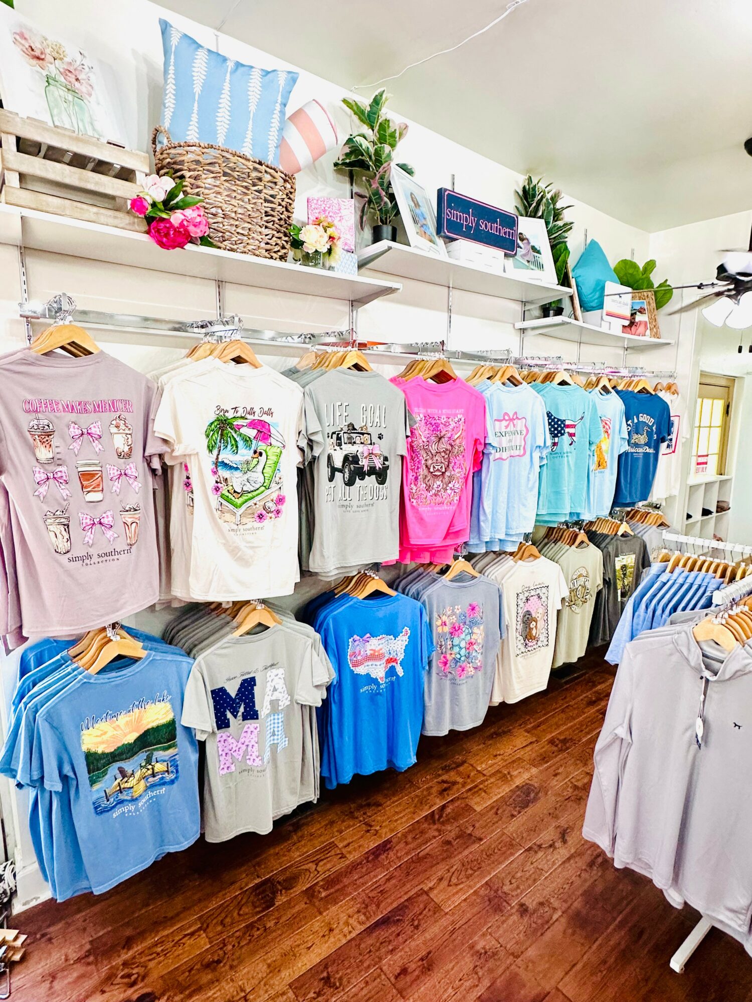Display of colorful children's T-shirts with various designs on a clothing rack in a store, with shelves and decorative items above.