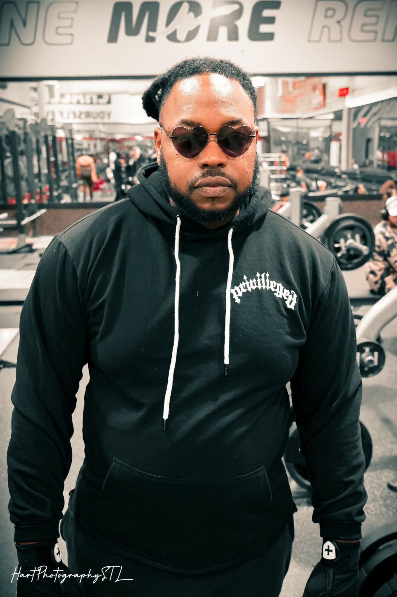 Man wearing sunglasses and a black hoodie with white text, standing in a store with bicycles and signs in the background.