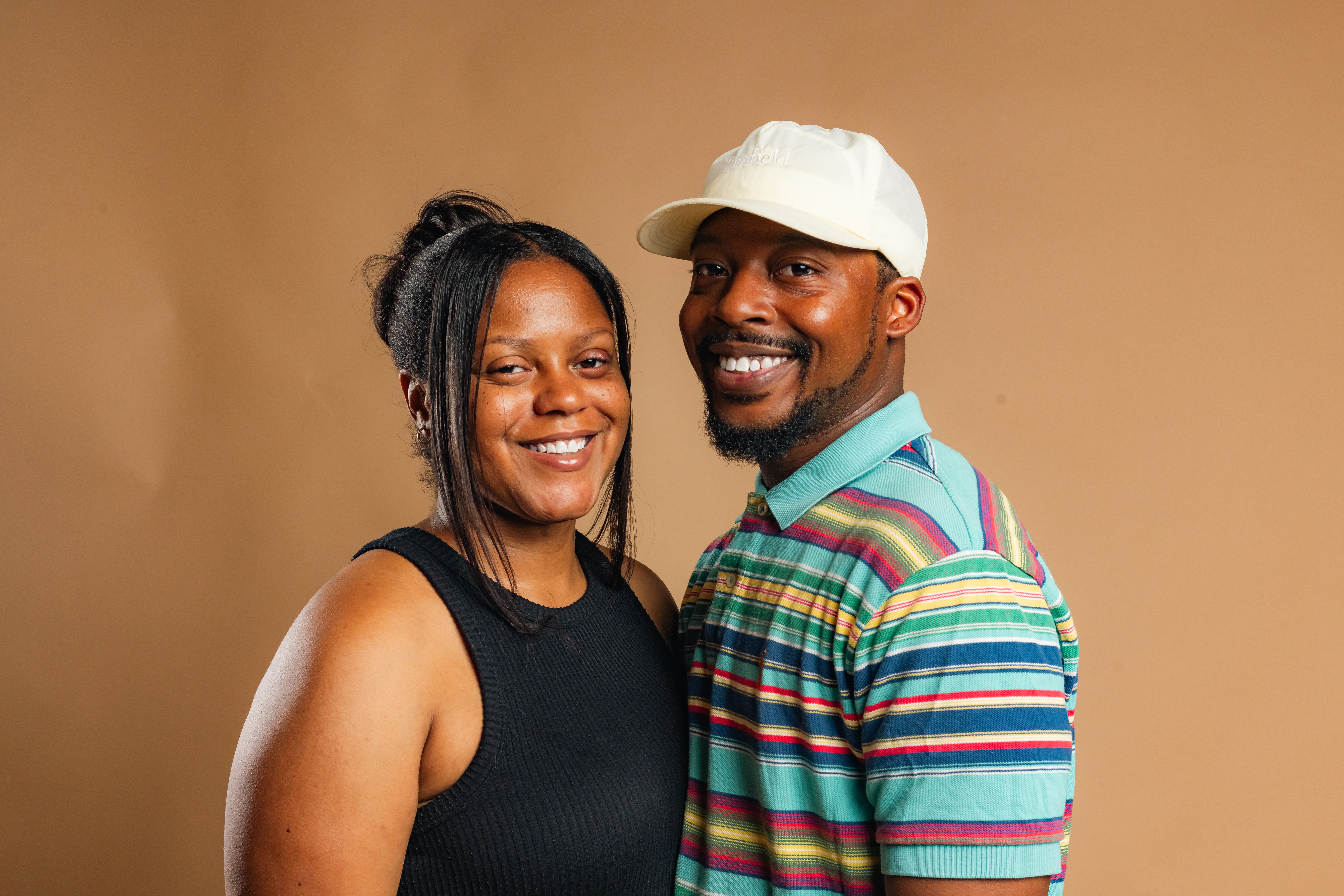 Two people smiling, standing close together, against a plain background.
