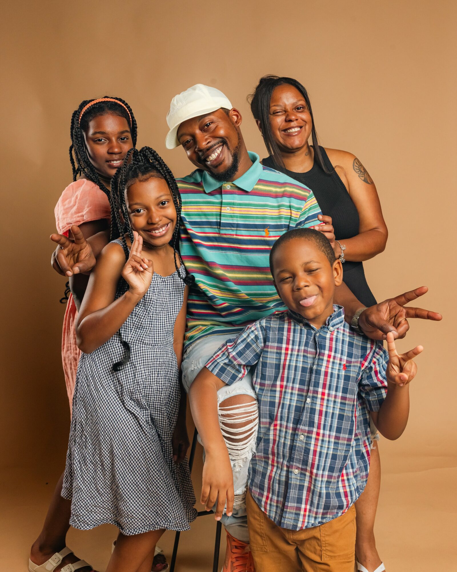 Group of five smiling people, including children and adults, posing together against a plain background.