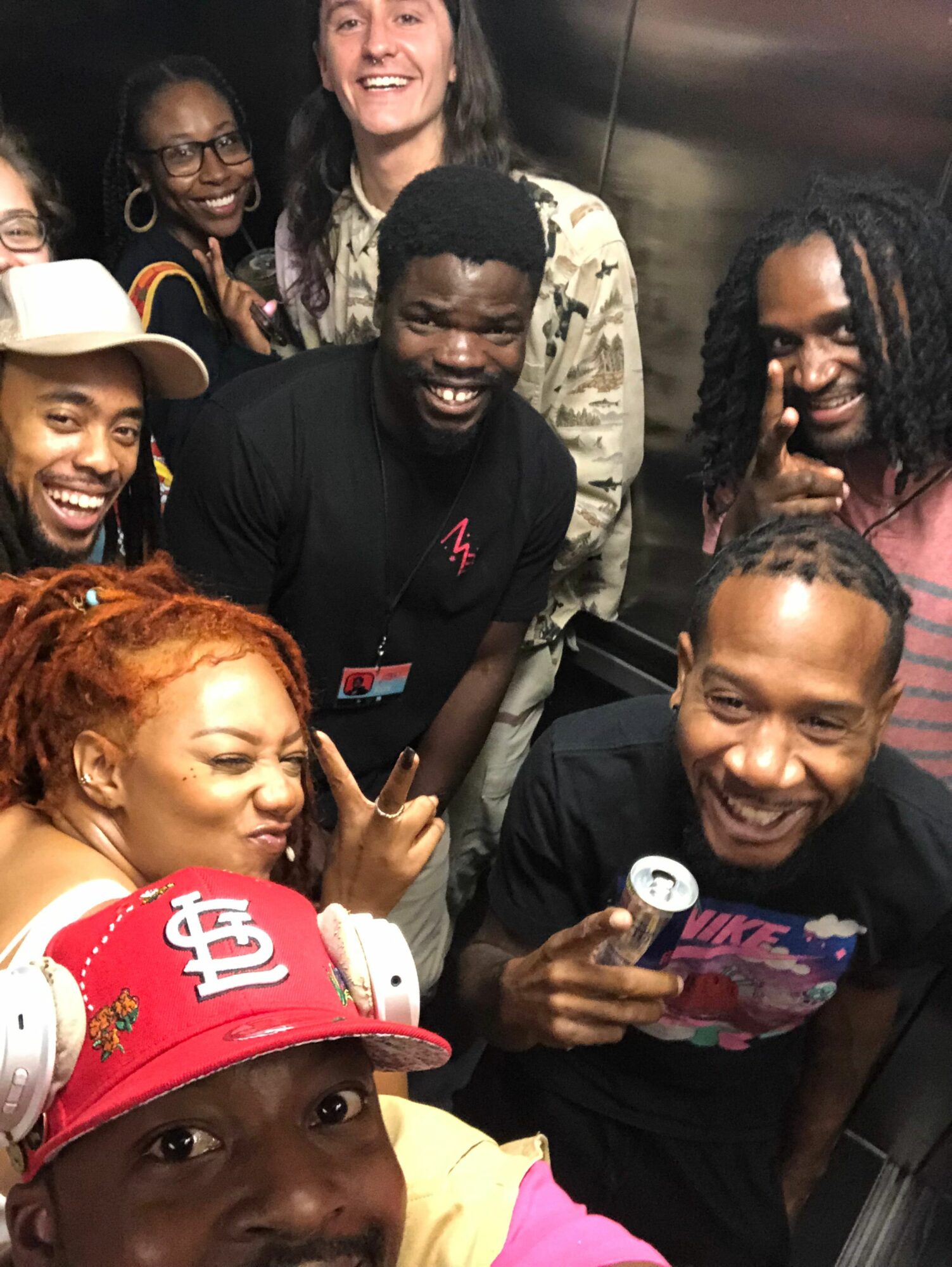 Group of six people smiling and posing for a photo, some making peace signs, in an indoor setting.