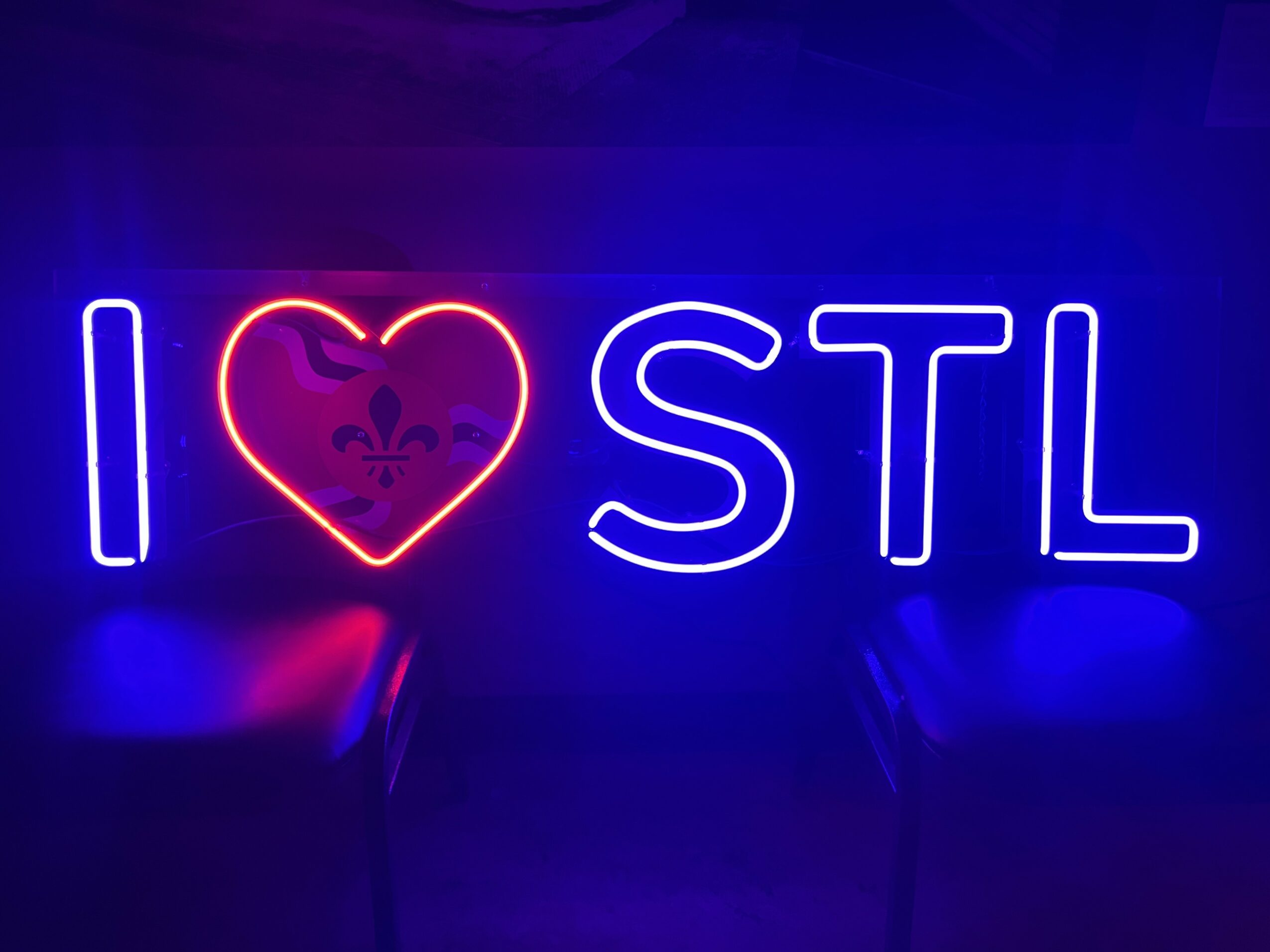 Neon sign reads 'I love STL' with a heart symbol, glowing in blue, red, and white colors.
