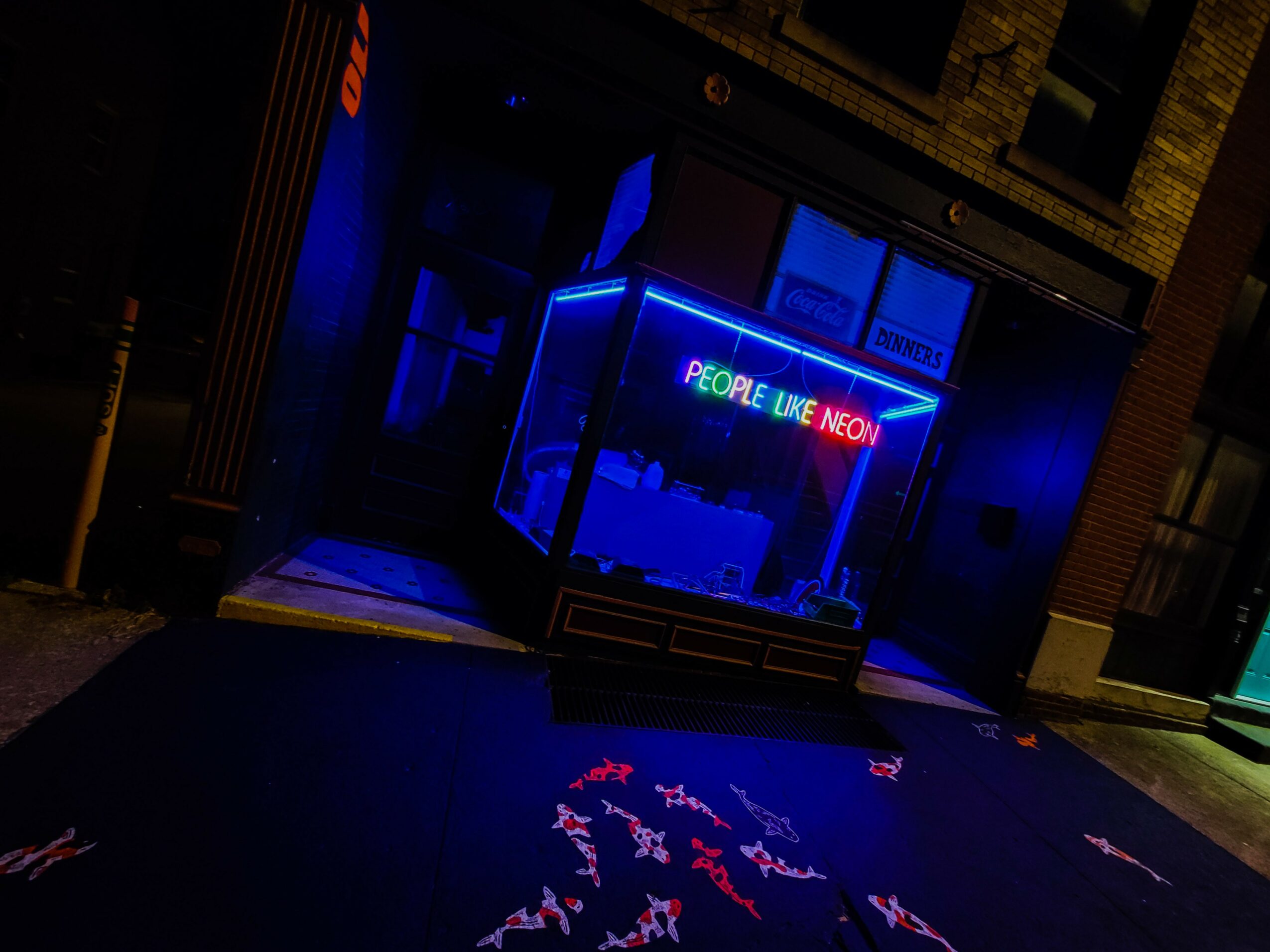 Nighttime storefront with neon sign reading 'People Like Info' in colorful letters, reflected on the sidewalk.