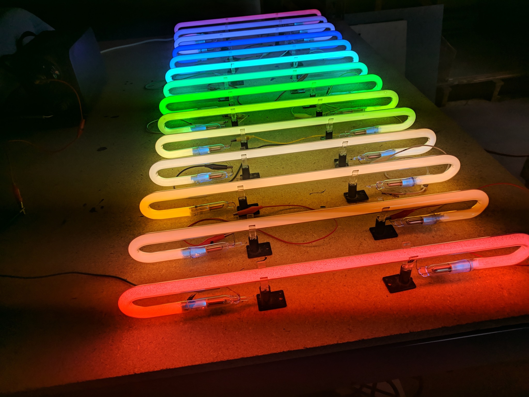 Colorful neon light tubes arranged in a row, glowing in rainbow colors on a dark surface.