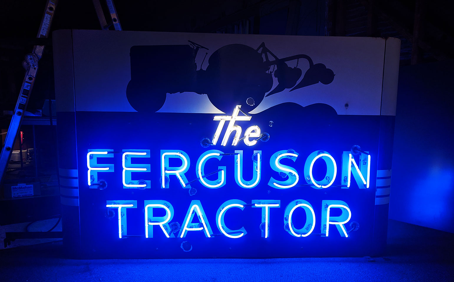 Illuminated blue neon sign reads 'The Ferguson Tractor' with a silhouette of a tractor above, against a dark background.