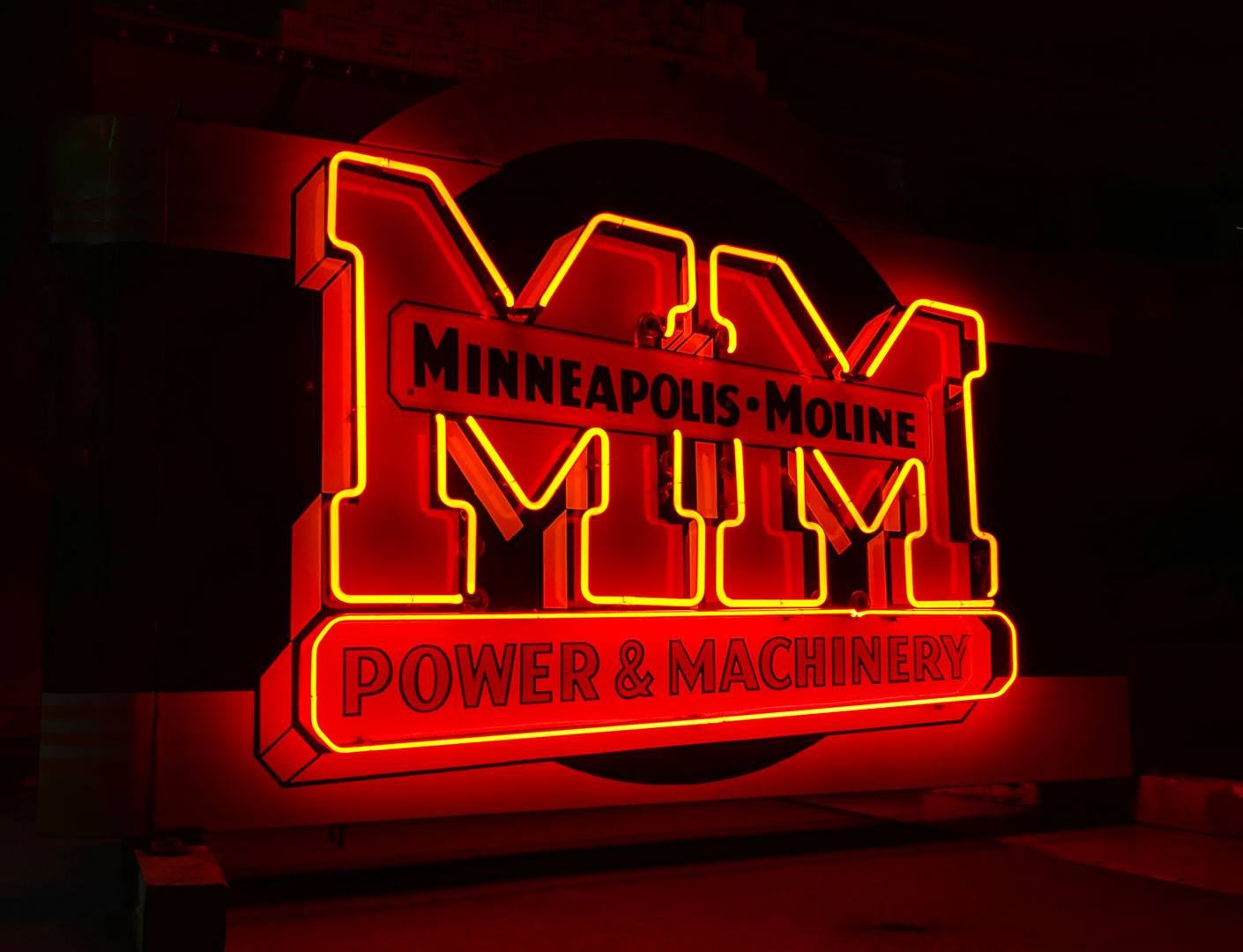 Neon sign with large letters reading 'MUM' and smaller text 'Minneapolis-Moline' and 'Power & Machinery' in red and yellow colors.