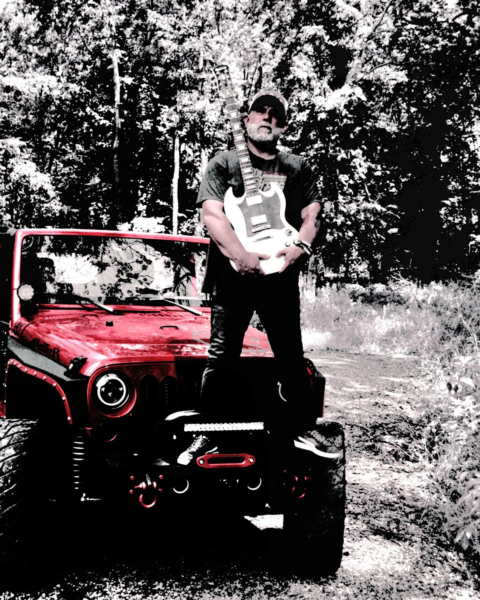 Person standing outdoors next to a red off-road vehicle, holding a helmet, with trees in the background.