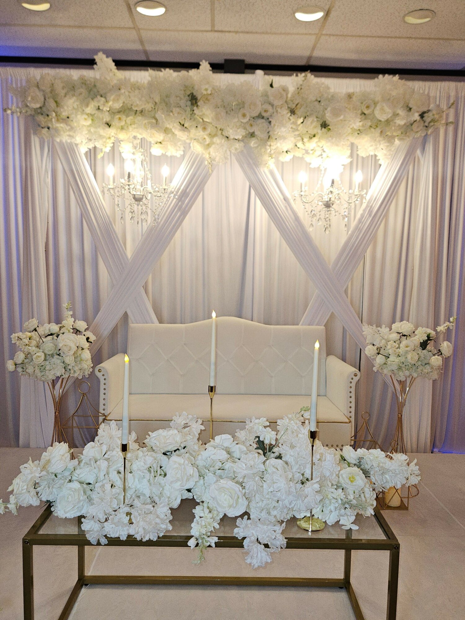 Elegant wedding backdrop with white flowers, draped fabric, and a seating area, decorated for a ceremony or reception.