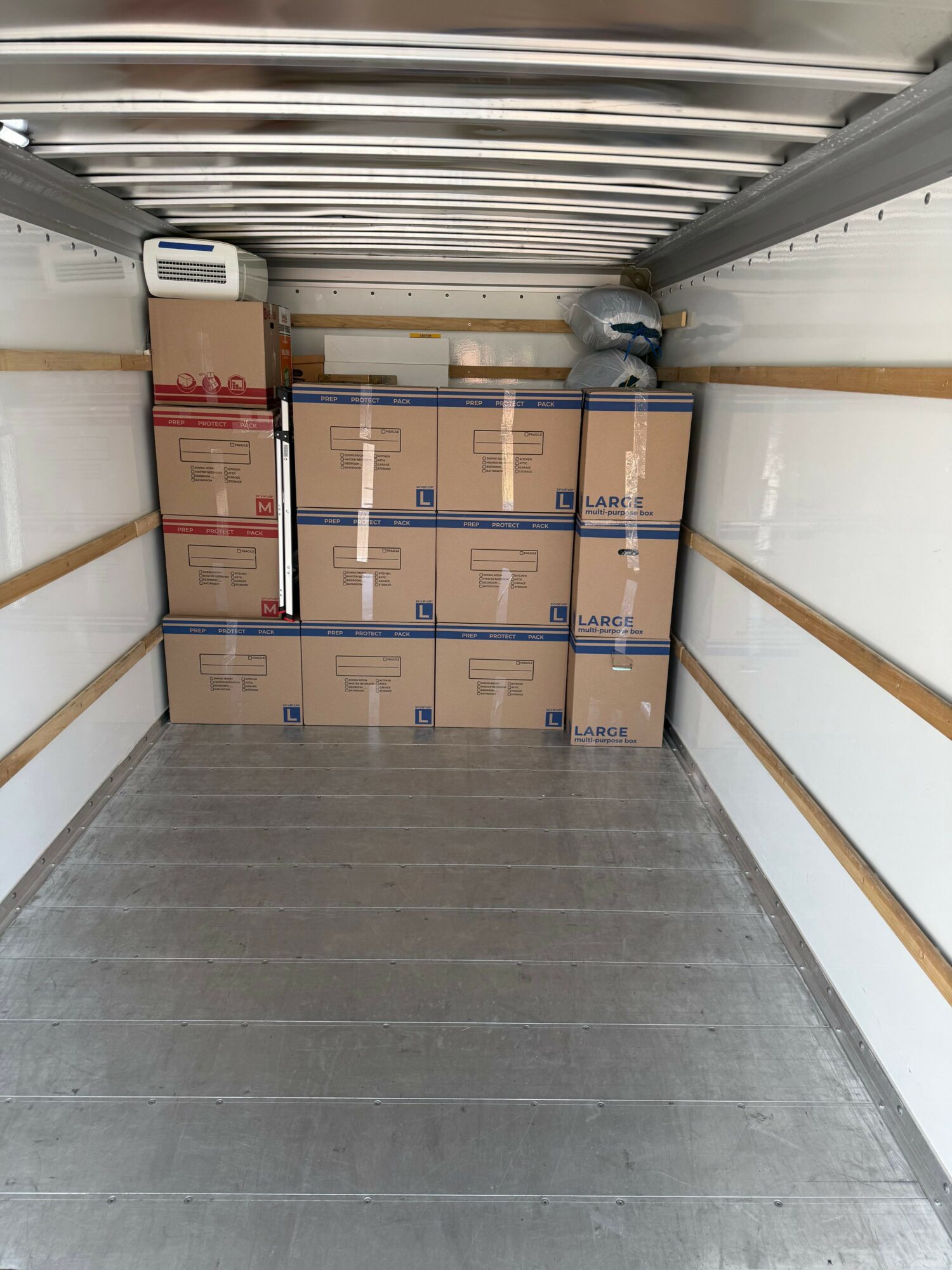 Boxes stacked in a storage room with metal walls and a concrete floor, viewed from the side.
