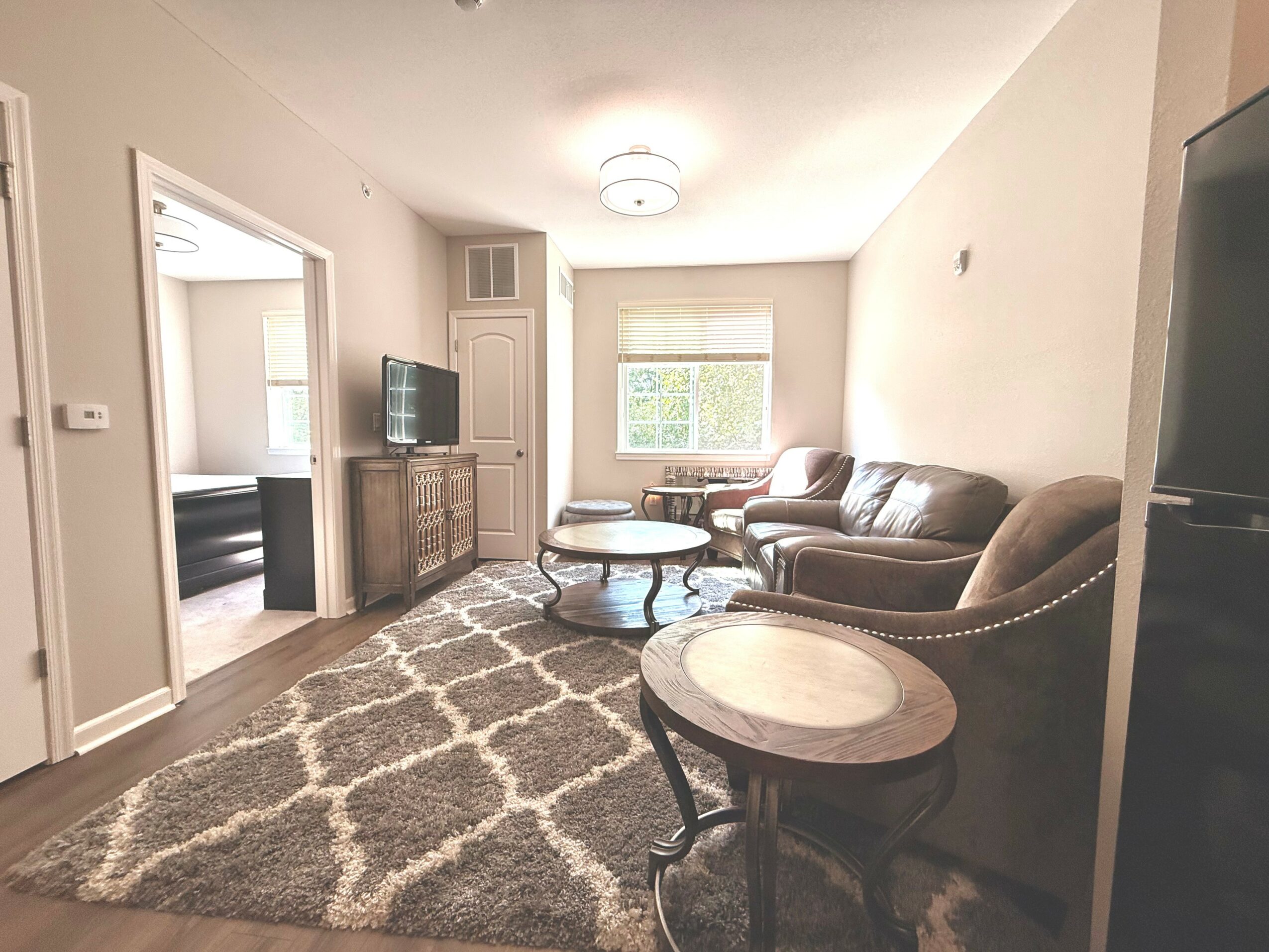 Living room with sofa, armchair, coffee table, window, and patterned rug, viewed from doorway.