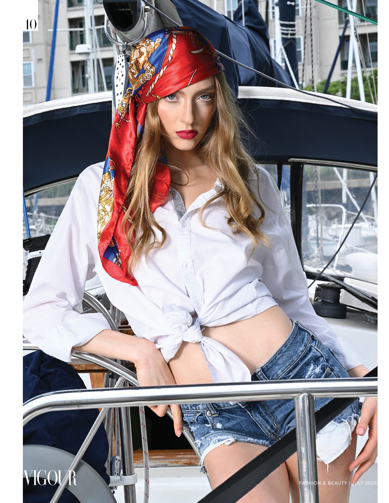 Young woman with long hair and red headscarf, wearing a white shirt and denim shorts, standing on a boat dock.