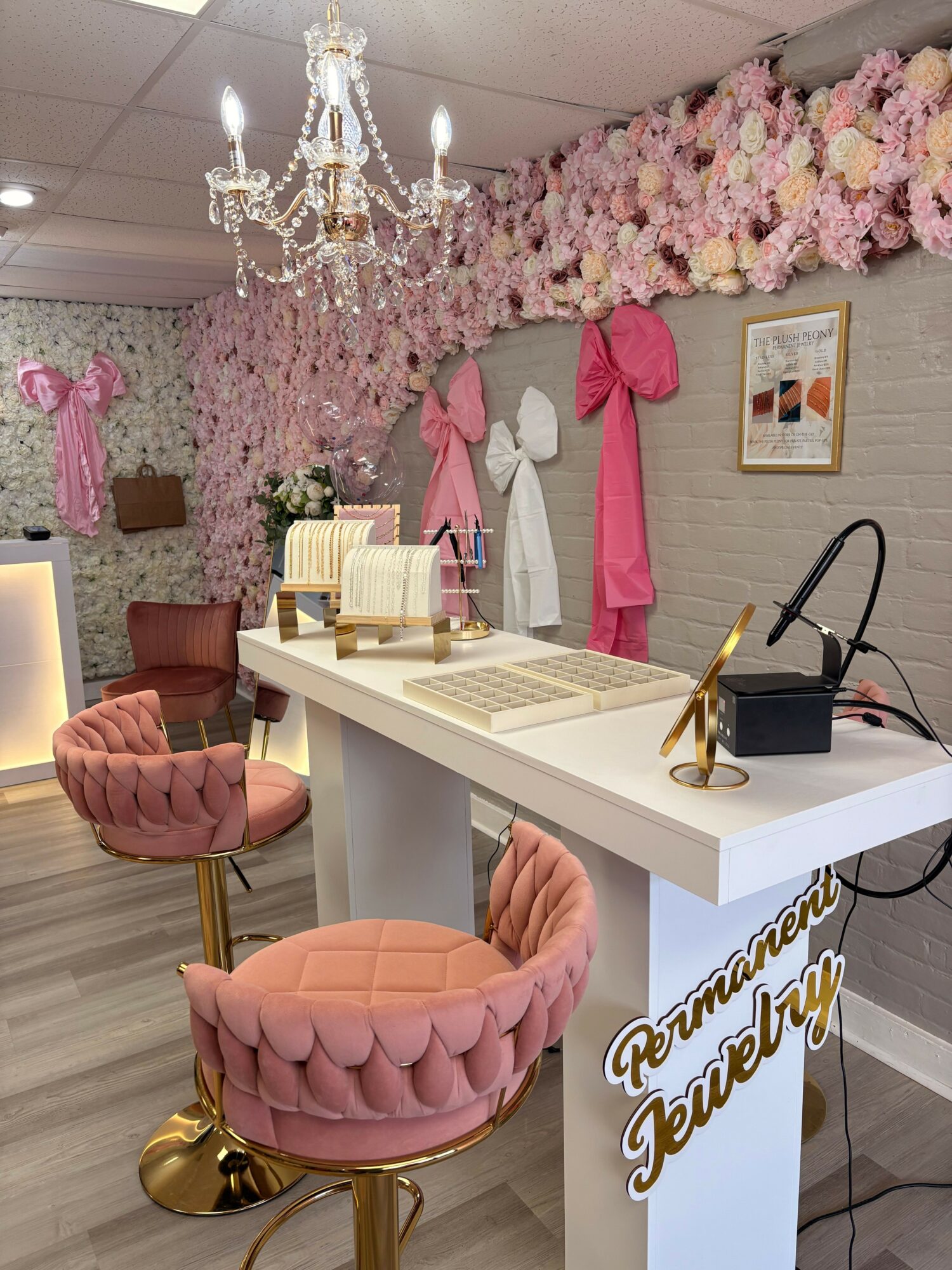 Decorative pink flowers, a white desk with books and accessories, pink tufted stool, and a chandelier in a stylish room.