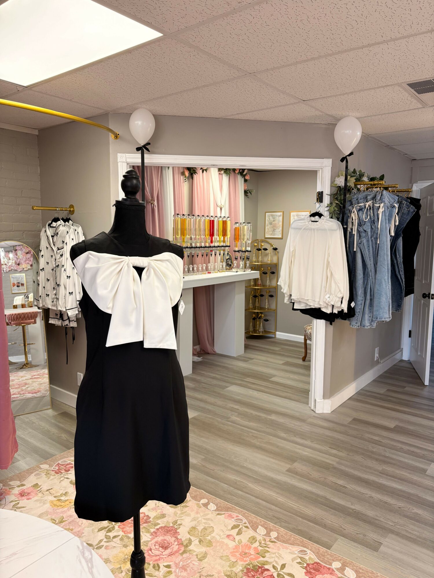 Person with black hair wearing a white top and black skirt standing in a room with shelves and clothing, facing away from the camera.