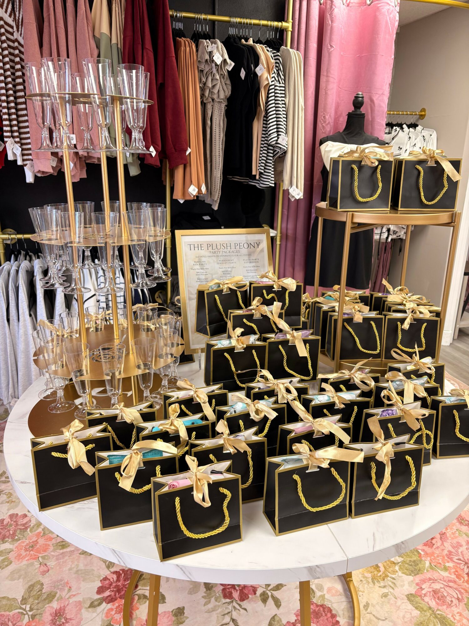 Display of black boxes with gold handles, pink and brown clothing items, and glassware on a table, with a floral carpet nearby.