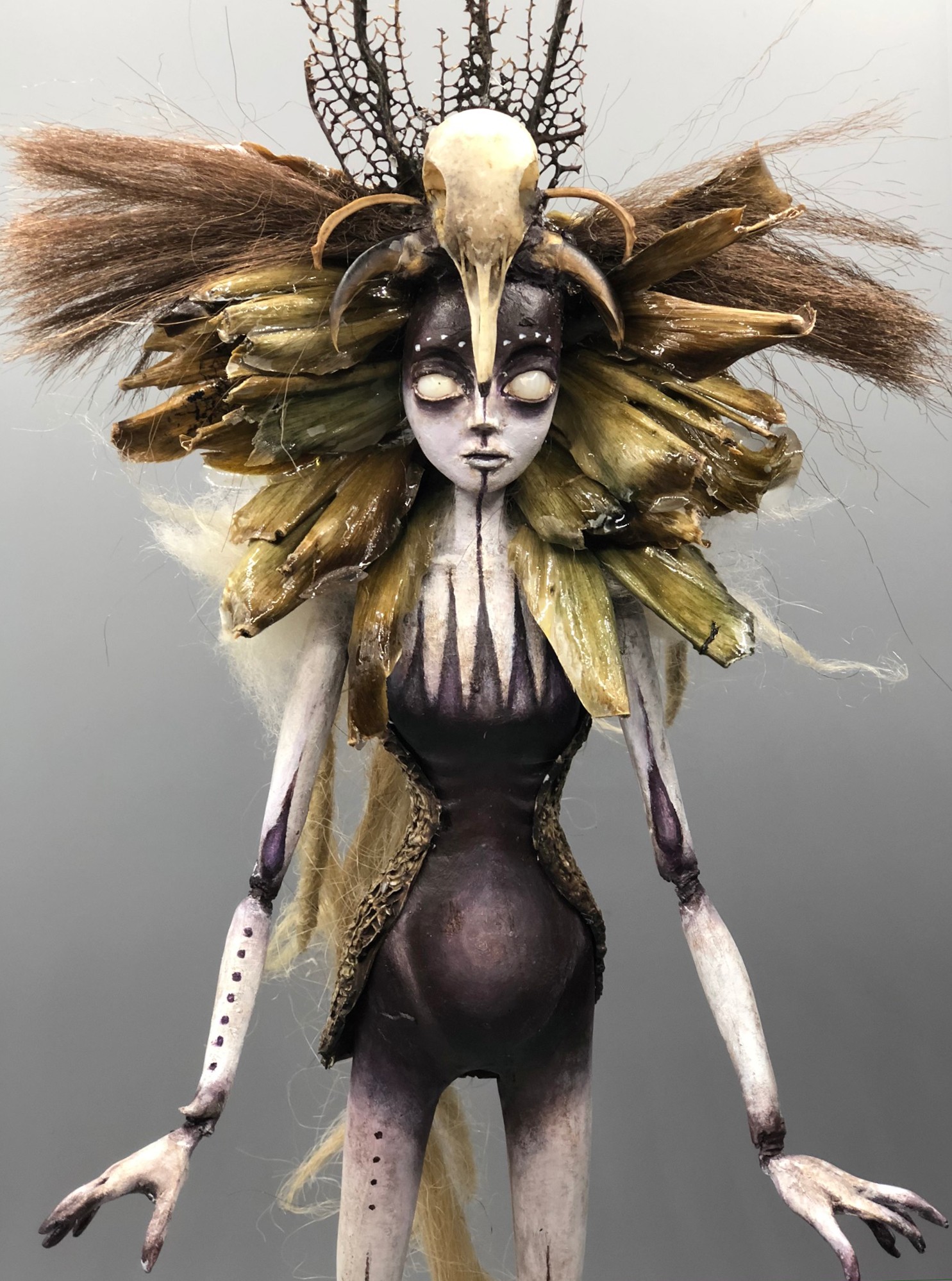 Fantasy creature with elaborate headdress, long arms, and a dark, textured body, standing against a plain background.
