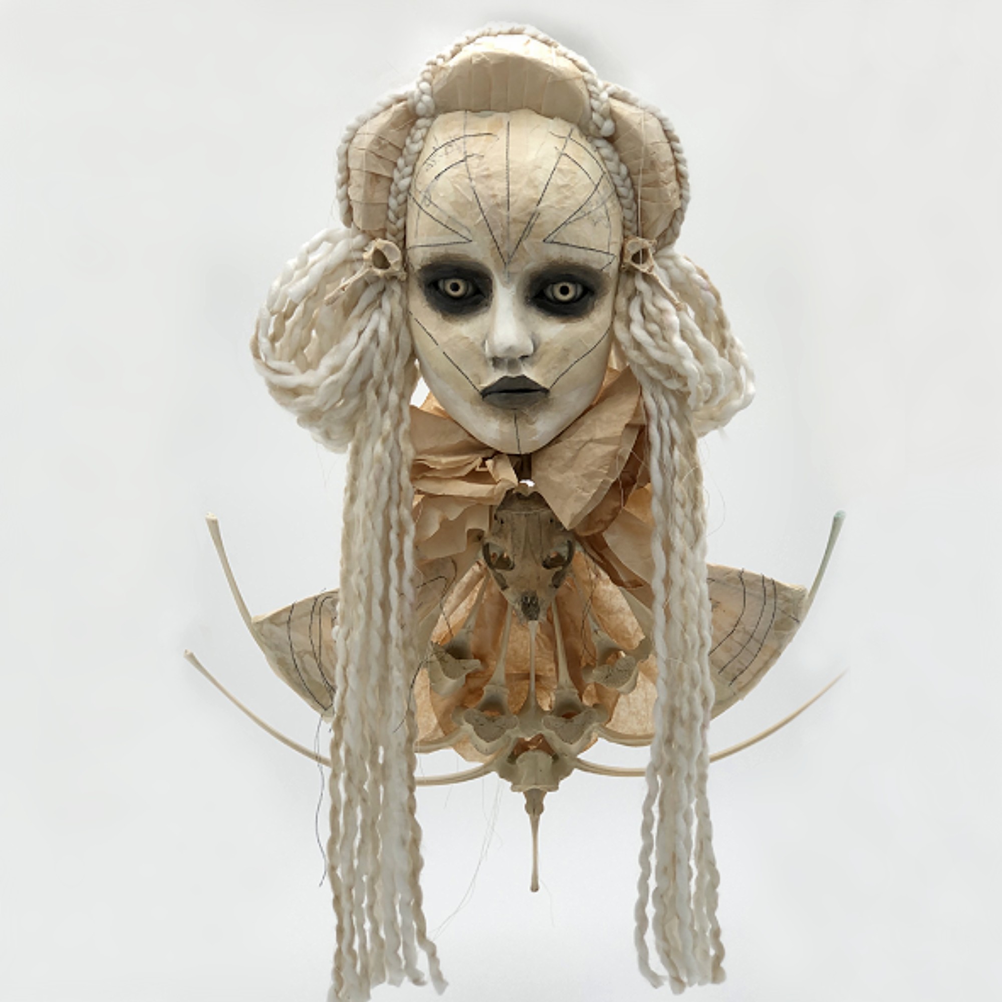 A detailed doll or sculpture of a female face with long, textured hair, wearing a ruffled collar and a decorative garment.