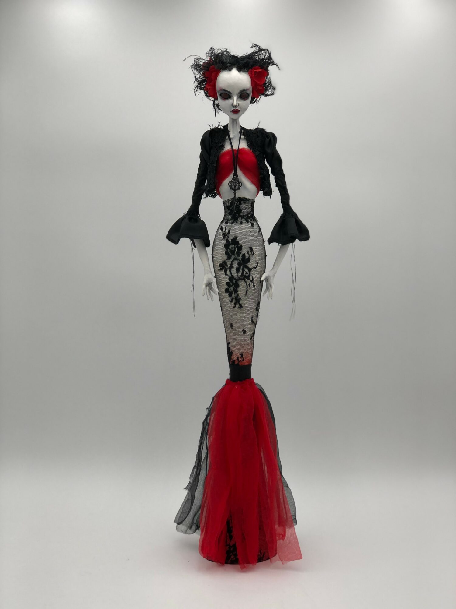 Tall doll with a gothic style, black and red dress, lace details, and a white face with dark makeup, standing against a plain background.