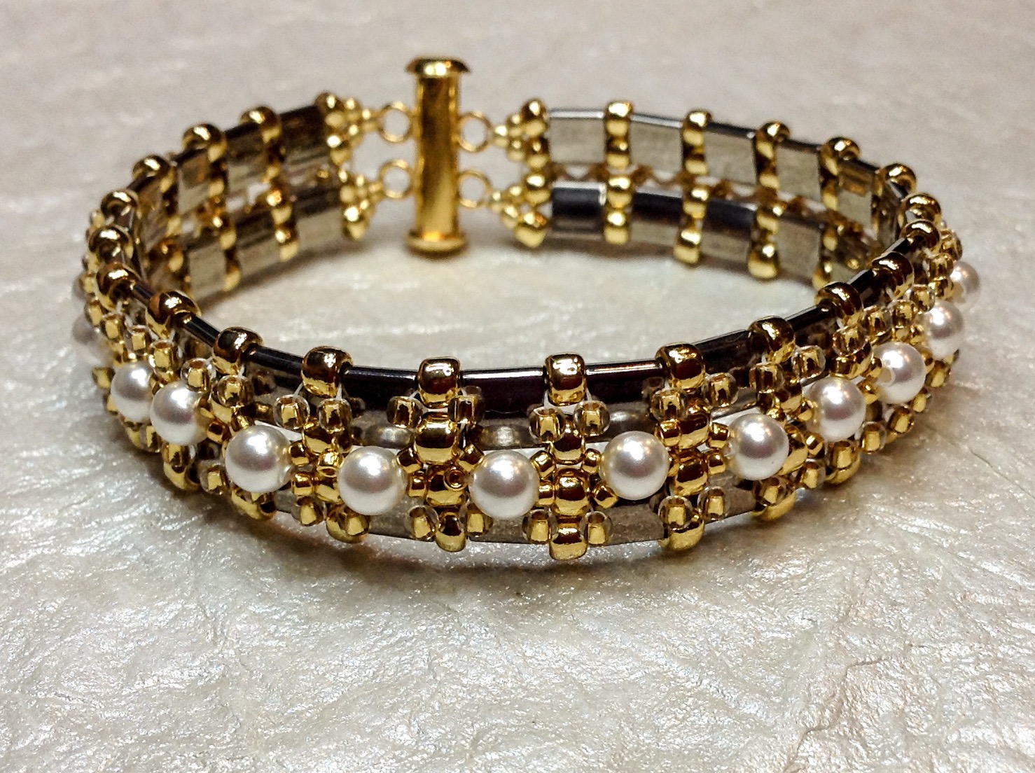 Gold and pearl bracelet with intricate design, resting on a textured surface.