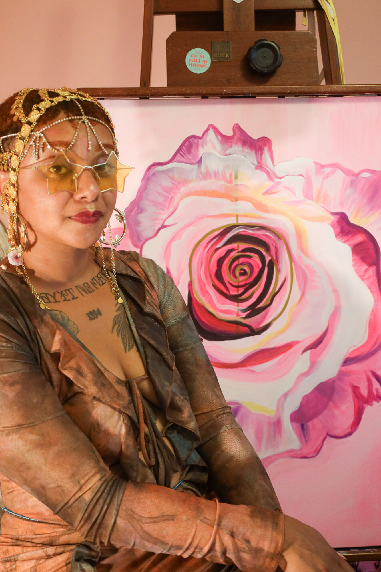Person with glasses and jewelry standing in front of a pink and white floral painting.