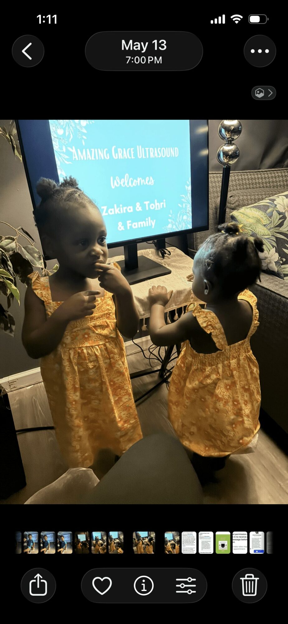 Two young children in yellow dresses holding hands and facing each other, standing in front of a television screen.