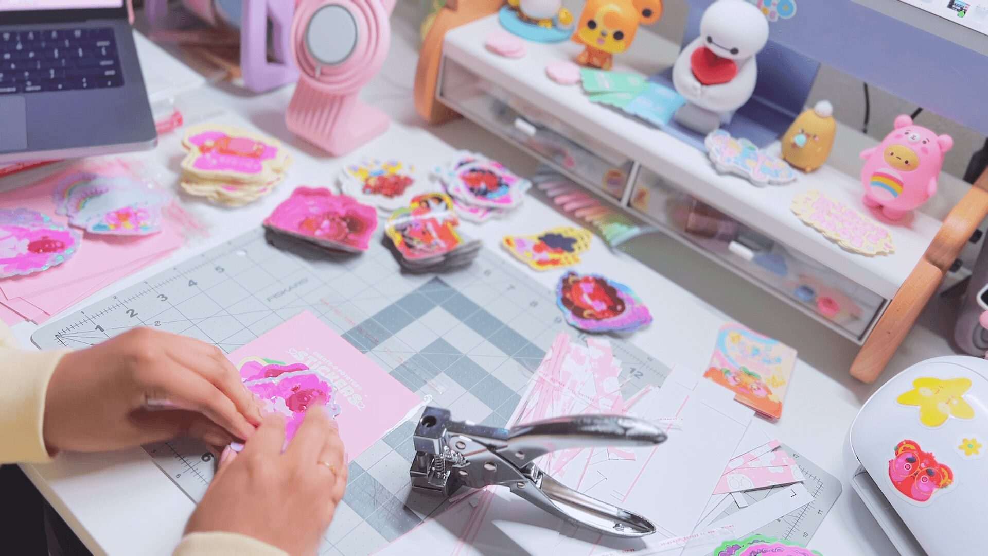 Hands working on pink craft projects with colorful toys and crafting supplies on a table.