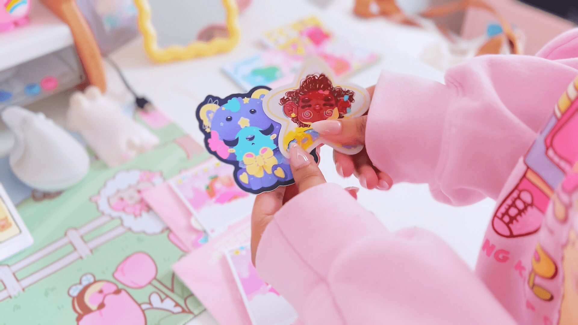 Person holding colorful cartoon character stickers, with a pink and pastel background of toys and decorations.